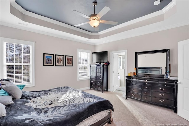 bedroom with connected bathroom, light carpet, ornamental molding, a tray ceiling, and ceiling fan