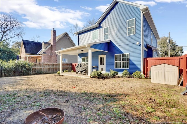 back of house featuring a shed, a fire pit, a patio area, and a lawn