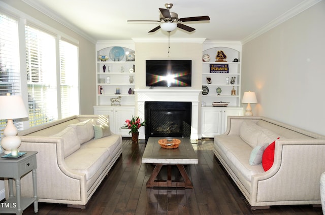 living room with built in shelves, ceiling fan, ornamental molding, and dark wood-type flooring