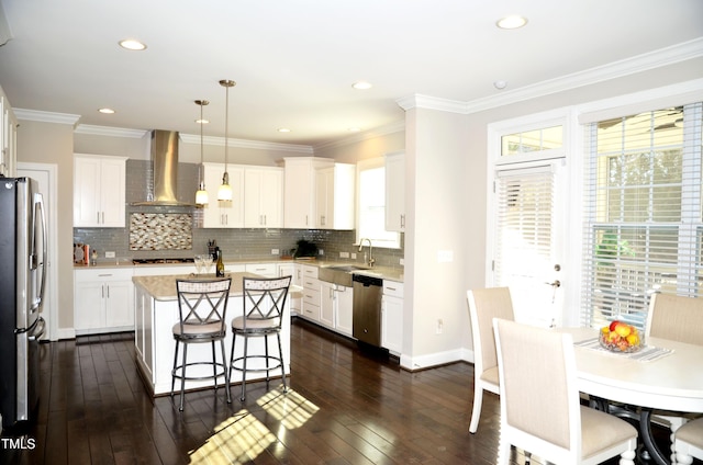 kitchen featuring pendant lighting, appliances with stainless steel finishes, a center island, white cabinets, and wall chimney exhaust hood