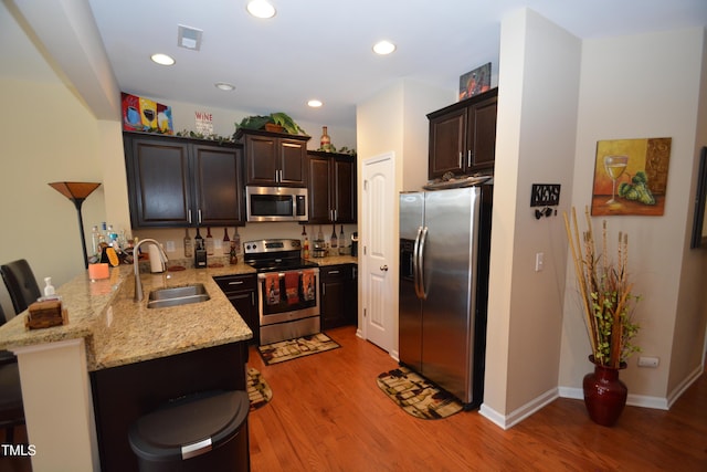 kitchen with sink, a kitchen breakfast bar, kitchen peninsula, stainless steel appliances, and light stone countertops