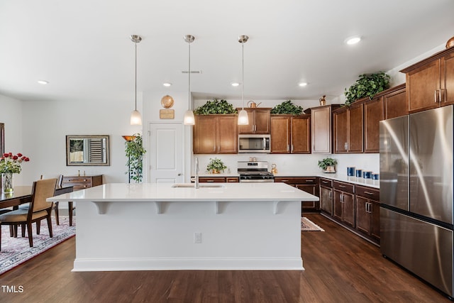 kitchen featuring sink, a breakfast bar, hanging light fixtures, stainless steel appliances, and an island with sink