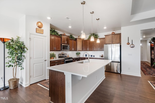 kitchen with a breakfast bar, sink, hanging light fixtures, appliances with stainless steel finishes, and an island with sink