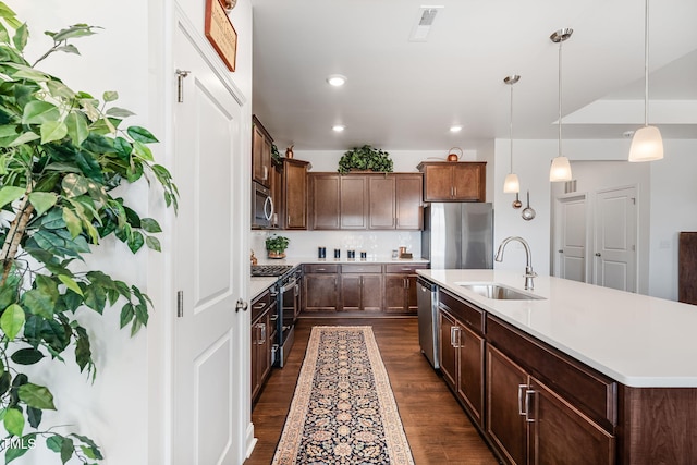 kitchen with an island with sink, sink, decorative backsplash, hanging light fixtures, and stainless steel appliances