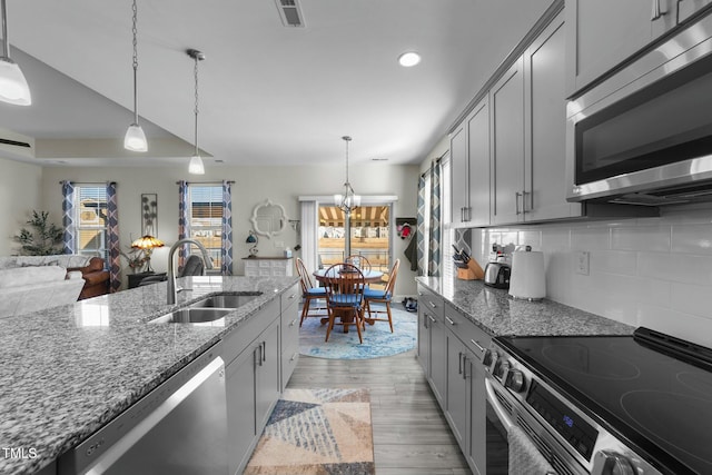 kitchen with sink, gray cabinetry, appliances with stainless steel finishes, pendant lighting, and light stone countertops