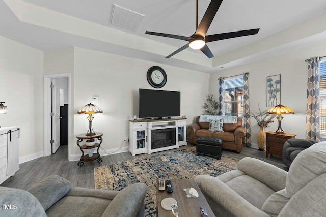 living room featuring dark wood-type flooring, a raised ceiling, and ceiling fan