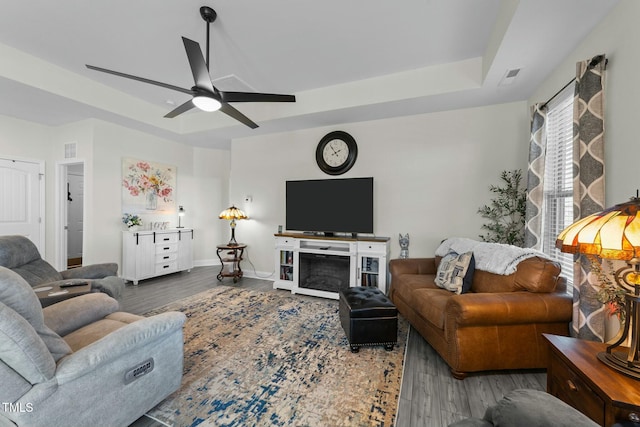 living room featuring a tray ceiling, a fireplace, ceiling fan, and hardwood / wood-style flooring