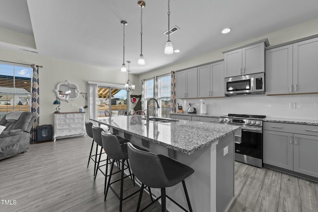 kitchen featuring sink, appliances with stainless steel finishes, a kitchen island with sink, hanging light fixtures, and a kitchen breakfast bar