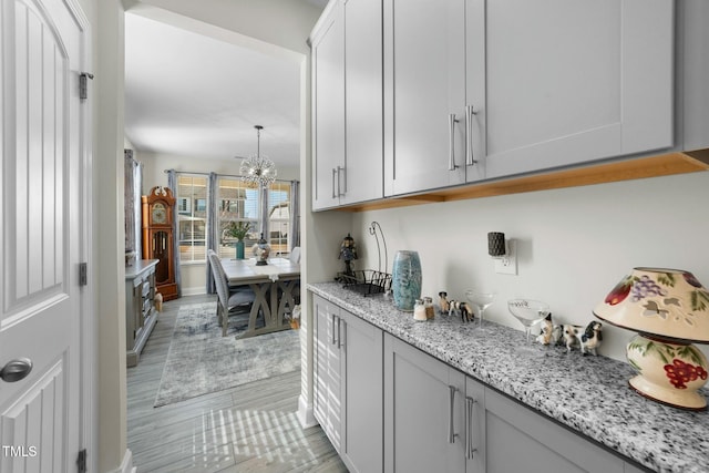 bar featuring light stone counters, white cabinetry, light hardwood / wood-style flooring, and a notable chandelier