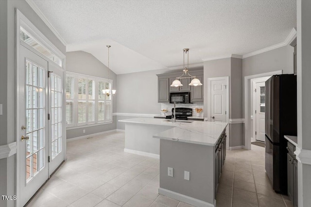 kitchen with sink, an inviting chandelier, light stone counters, an island with sink, and black appliances