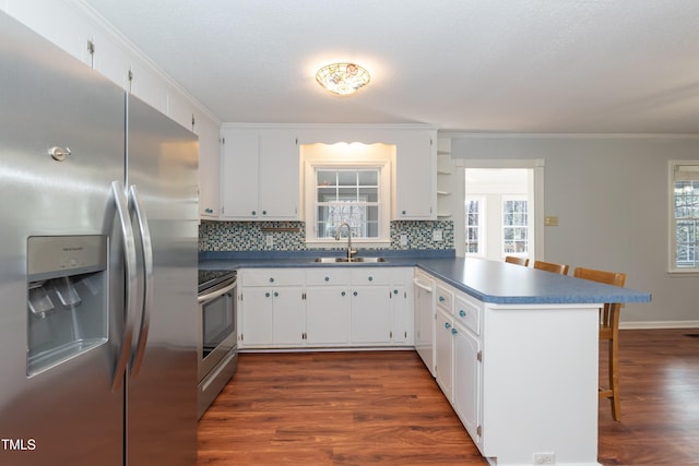 kitchen with stainless steel appliances, a peninsula, white cabinets, dark countertops, and a kitchen bar