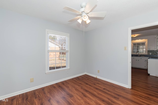 unfurnished room with dark wood-type flooring, a sink, baseboards, and ceiling fan