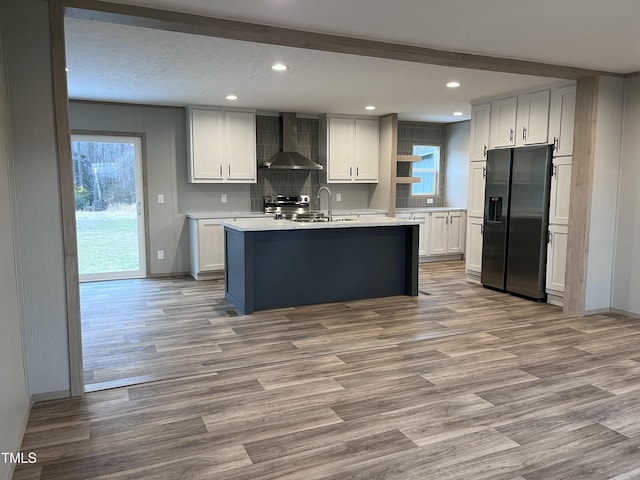 kitchen with stainless steel appliances, a kitchen island with sink, white cabinets, and wall chimney exhaust hood