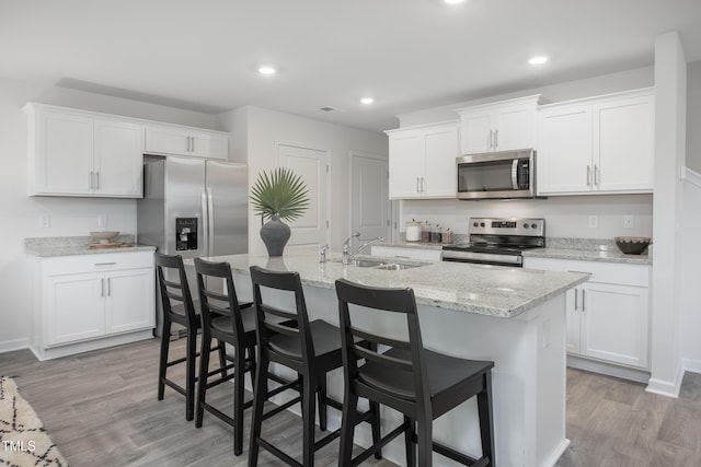 kitchen with sink, appliances with stainless steel finishes, white cabinets, a center island with sink, and light wood-type flooring