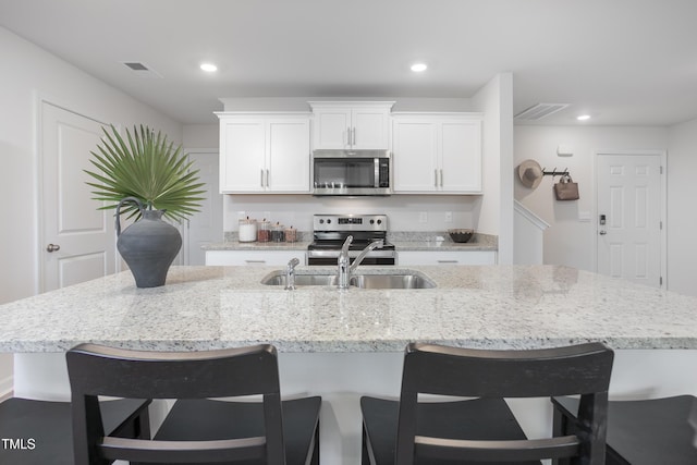 kitchen with sink, a breakfast bar area, white cabinetry, stainless steel appliances, and a kitchen island with sink