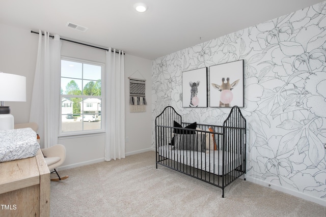 bedroom featuring a nursery area, light colored carpet, and a large fireplace