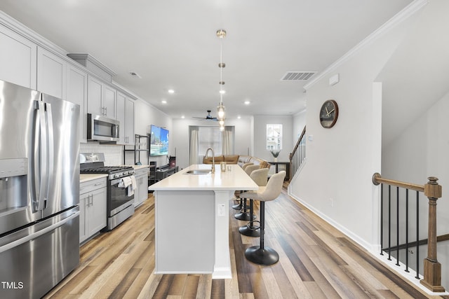 kitchen with sink, appliances with stainless steel finishes, an island with sink, pendant lighting, and backsplash