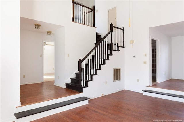 stairway with hardwood / wood-style flooring, a towering ceiling, and ceiling fan