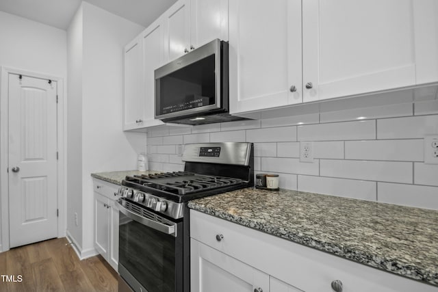 kitchen featuring dark wood-type flooring, white cabinetry, tasteful backsplash, dark stone countertops, and stainless steel appliances