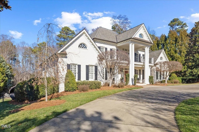 neoclassical / greek revival house featuring driveway, fence, and a balcony