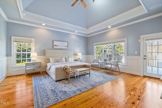 bedroom with access to exterior, a tray ceiling, light wood finished floors, and wainscoting