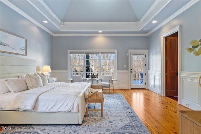 bedroom with a wainscoted wall, access to outside, a tray ceiling, and light wood-type flooring