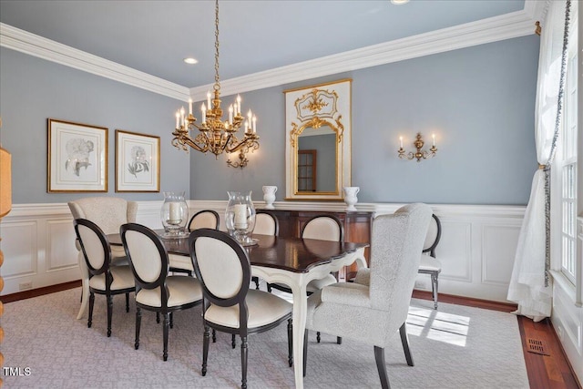 dining space featuring a wainscoted wall, an inviting chandelier, crown molding, light wood-type flooring, and a decorative wall