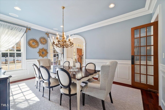 dining space featuring wainscoting, dark wood-style floors, ornamental molding, a chandelier, and a decorative wall