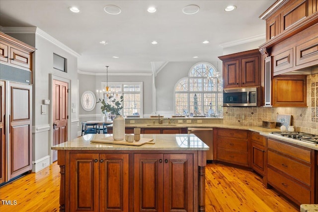 kitchen with crown molding, a sink, appliances with stainless steel finishes, a center island, and pendant lighting