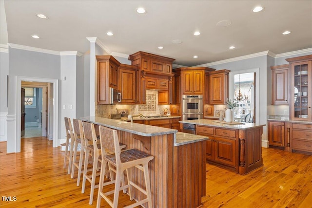 kitchen featuring light stone counters, brown cabinets, appliances with stainless steel finishes, a peninsula, and a kitchen bar