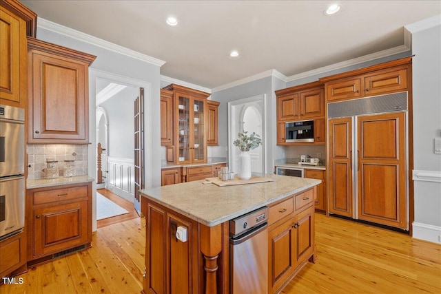 kitchen with arched walkways, stainless steel double oven, paneled built in refrigerator, brown cabinets, and glass insert cabinets