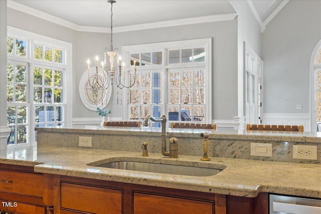 kitchen with a sink, ornamental molding, light stone countertops, brown cabinetry, and pendant lighting