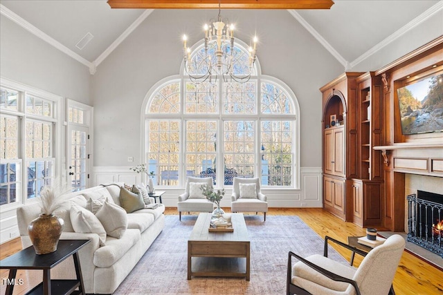 living room with light wood finished floors, a wainscoted wall, a lit fireplace, crown molding, and a chandelier