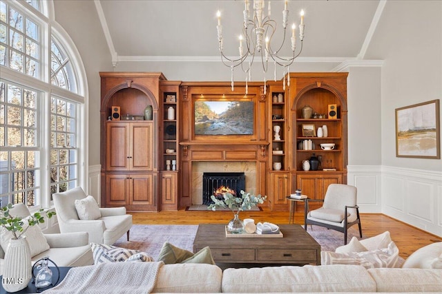 living room with an inviting chandelier, ornamental molding, a premium fireplace, wainscoting, and light wood-type flooring