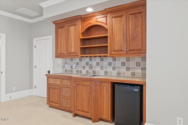 kitchen featuring a sink, fridge, backsplash, brown cabinetry, and crown molding