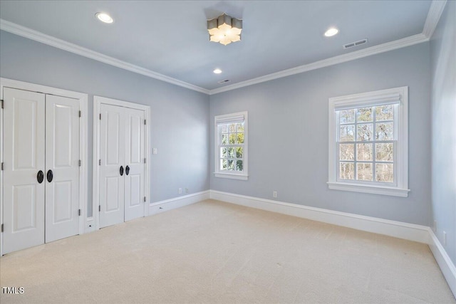 unfurnished bedroom with crown molding, visible vents, two closets, and light colored carpet