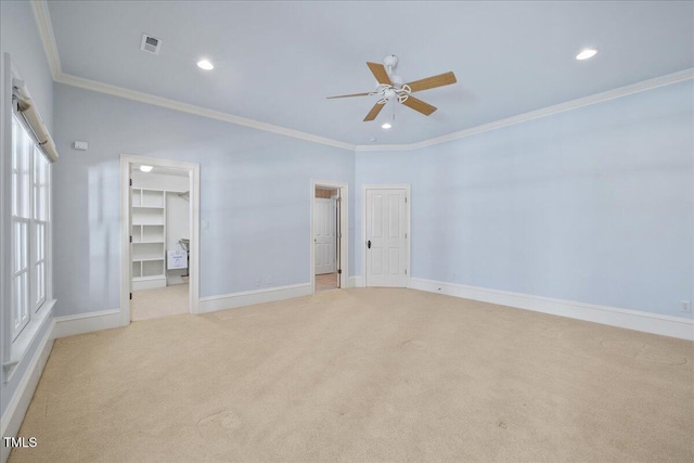 unfurnished bedroom with light carpet, visible vents, baseboards, ornamental molding, and a walk in closet