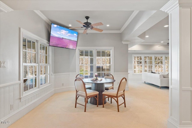 dining area with a wainscoted wall, ceiling fan, ornamental molding, and light colored carpet