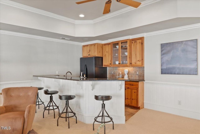 kitchen featuring a breakfast bar, brown cabinets, light colored carpet, black refrigerator with ice dispenser, and glass insert cabinets