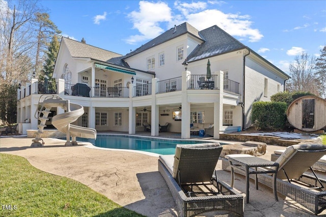 back of house featuring an outdoor pool, a patio, a balcony, and ceiling fan