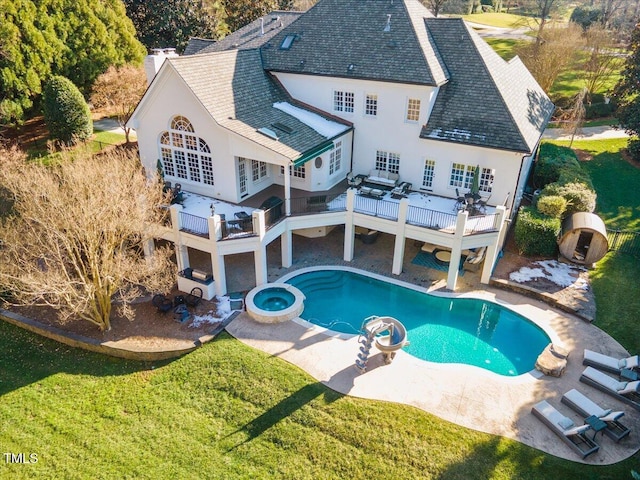 rear view of property featuring a lawn, a chimney, roof with shingles, a pool with connected hot tub, and stucco siding