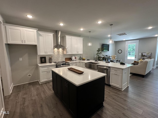 kitchen with white cabinetry, wall chimney range hood, a kitchen island, and appliances with stainless steel finishes