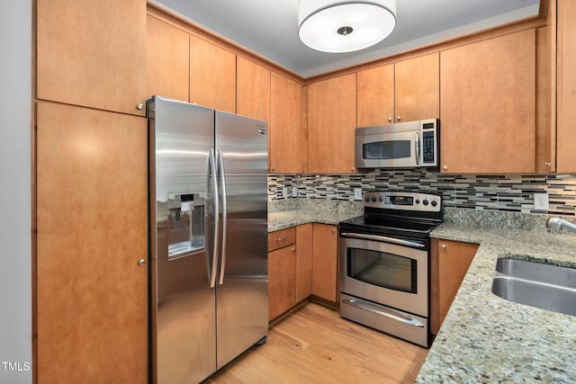 kitchen with sink, light wood-type flooring, light stone countertops, and appliances with stainless steel finishes