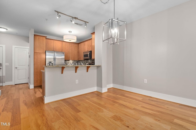 kitchen with backsplash, hanging light fixtures, kitchen peninsula, stainless steel appliances, and light hardwood / wood-style flooring