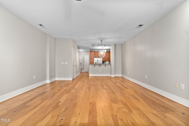 unfurnished living room featuring a notable chandelier and light hardwood / wood-style floors