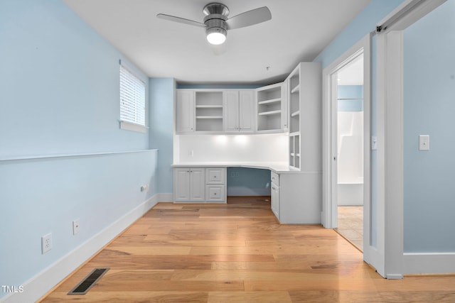 unfurnished office featuring light hardwood / wood-style flooring, built in desk, and ceiling fan