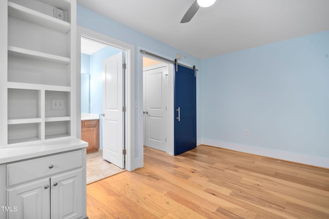 empty room with built in shelves, ceiling fan, a barn door, and light hardwood / wood-style floors