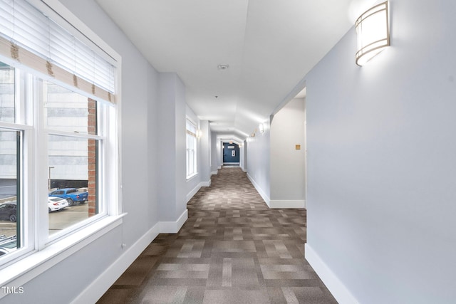 corridor featuring dark carpet and a wealth of natural light