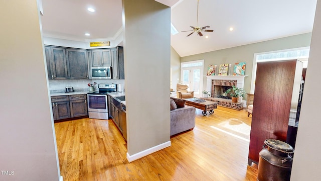 kitchen featuring light hardwood / wood-style flooring, ceiling fan, stainless steel appliances, tasteful backsplash, and a brick fireplace