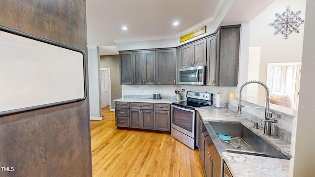 kitchen featuring dark brown cabinetry, stainless steel appliances, light stone countertops, and sink